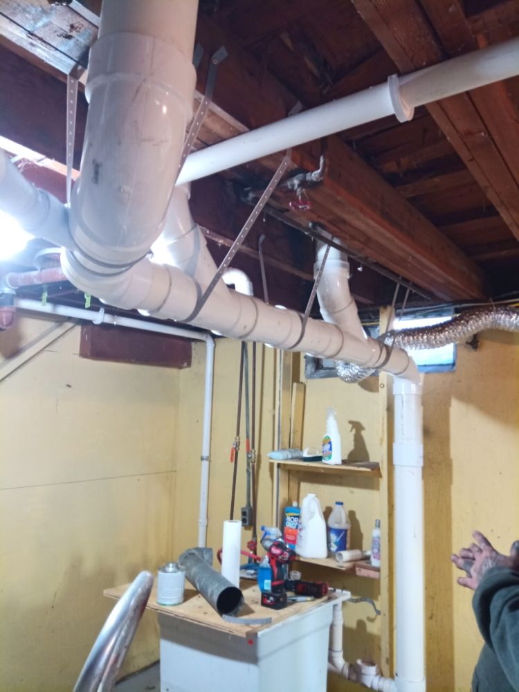 A fresh white PVC drain repipe running through the basement joists