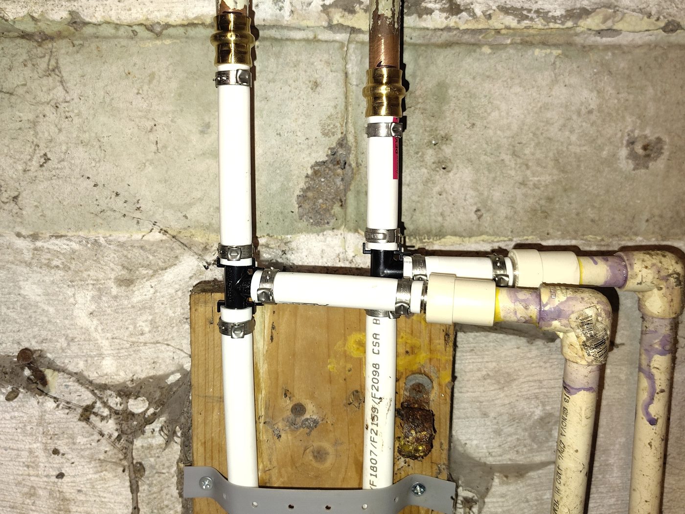 New white PEX joined to old copper and galvanized lines with brass push-fit couplings on a block basement wall