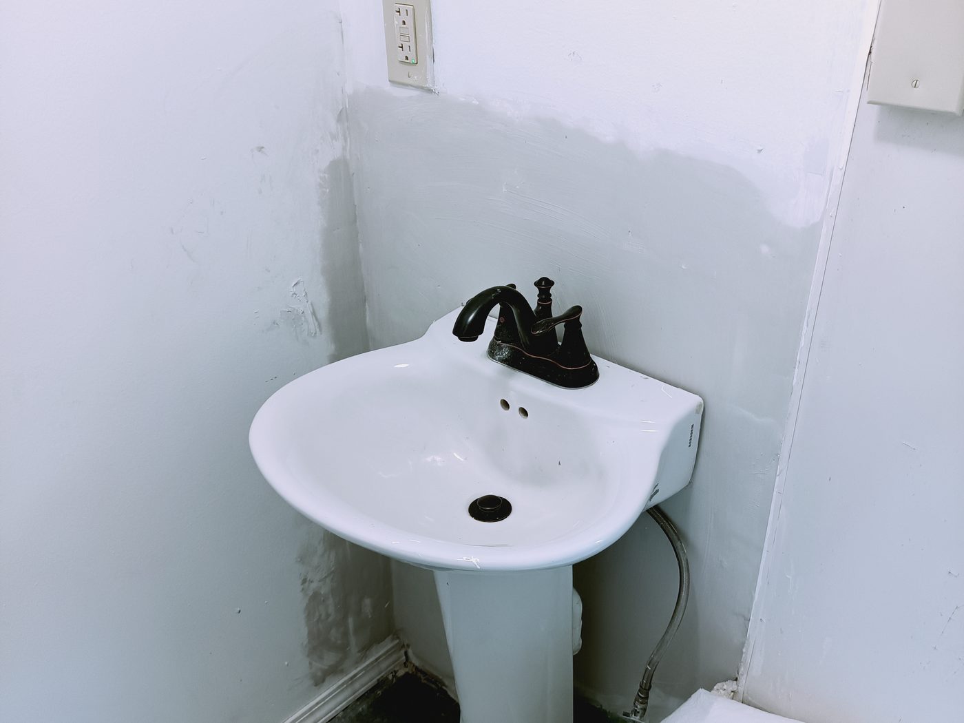 A newly installed pedestal sink with a bronze faucet in a repainted Flint bathroom